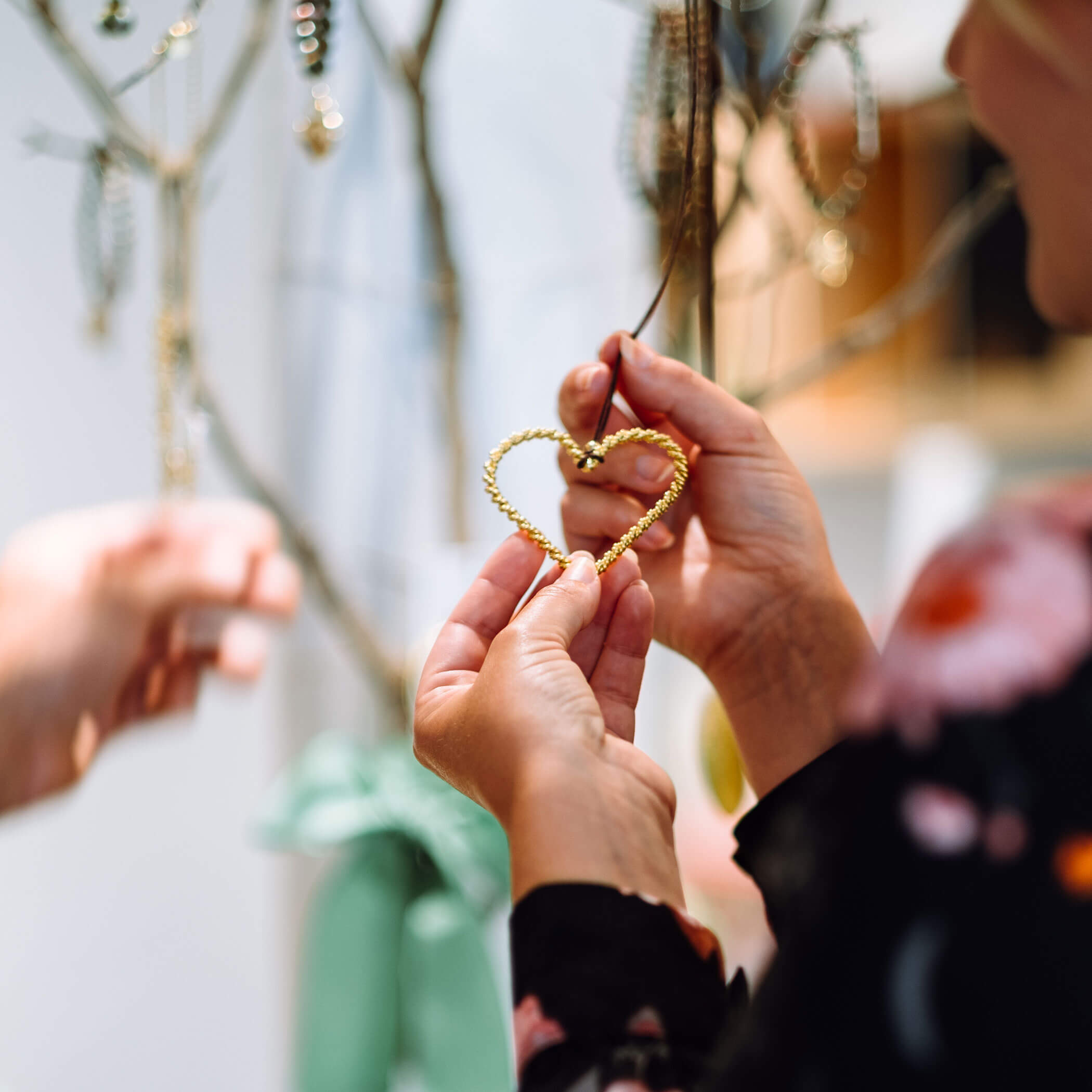 Hände, die ein goldenes herzförmiges Ornament in der Nähe eines mit einem grünen Band geschmückten Astes halten. - Hotel Sun