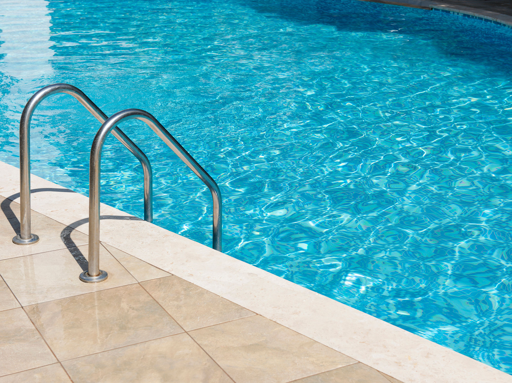Metallleiter, die an einem sonnigen Tag neben einer gefliesten Terrasse in ein klares blaues Schwimmbecken führt. - Hotel Sun