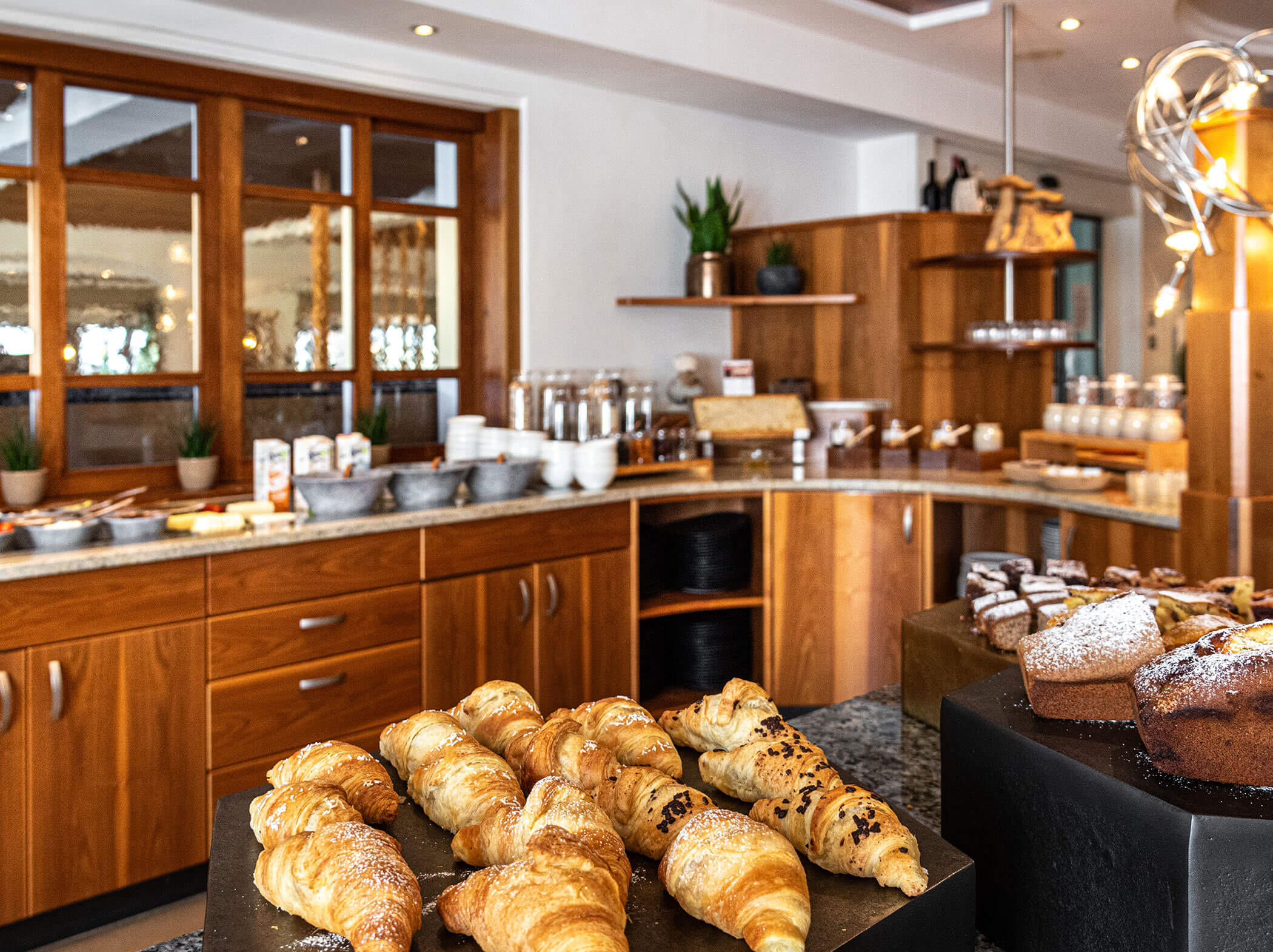 An einem Buffet mit Holzschränken und verschiedenen Frühstücksangeboten werden verschiedene Backwaren und Croissants angeboten. - Hotel Sun