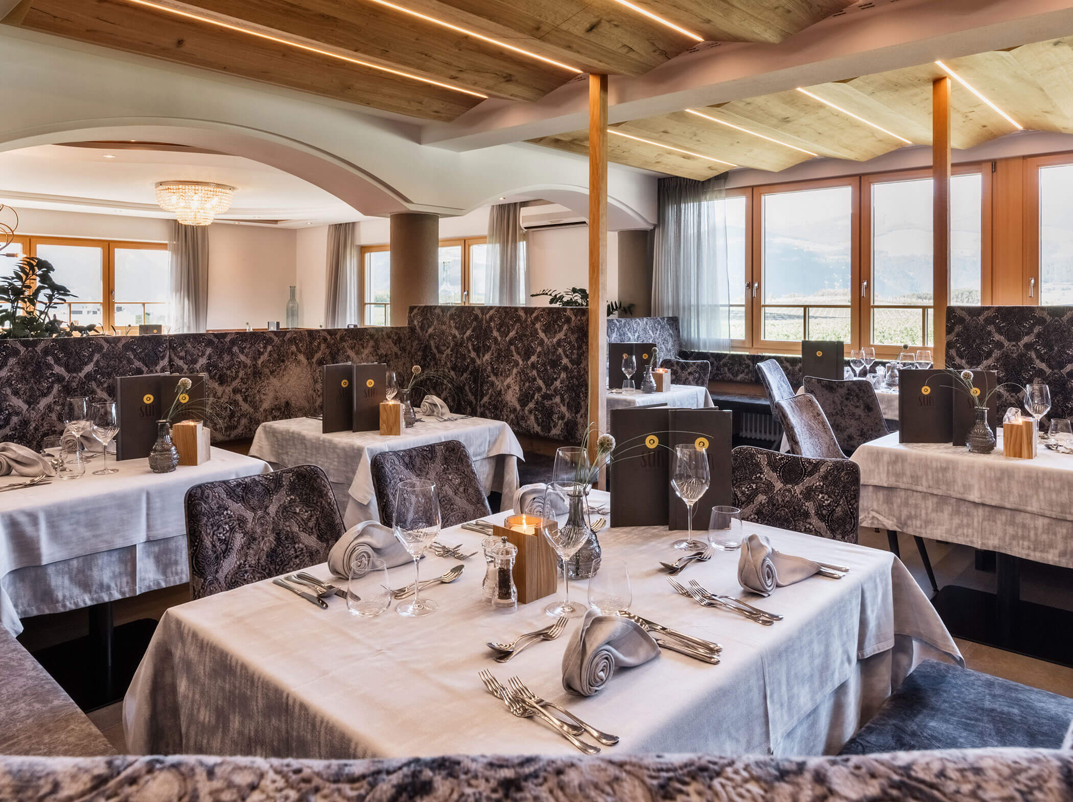 Elegant restaurant dining area with set tables, plush seating, large windows, and soft natural lighting. - Hotel Sun