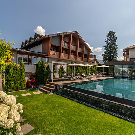 Modernes Hotel mit Holzbalkonen, Pool, Liegestühlen und grünem Garten unter strahlend blauem Himmel. - Hotel Sun