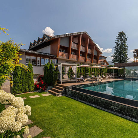 Ein modernes alpines Hotel mit Balkonen, Garten und Außenpool unter einem sonnigen blauen Himmel. - Hotel Sun