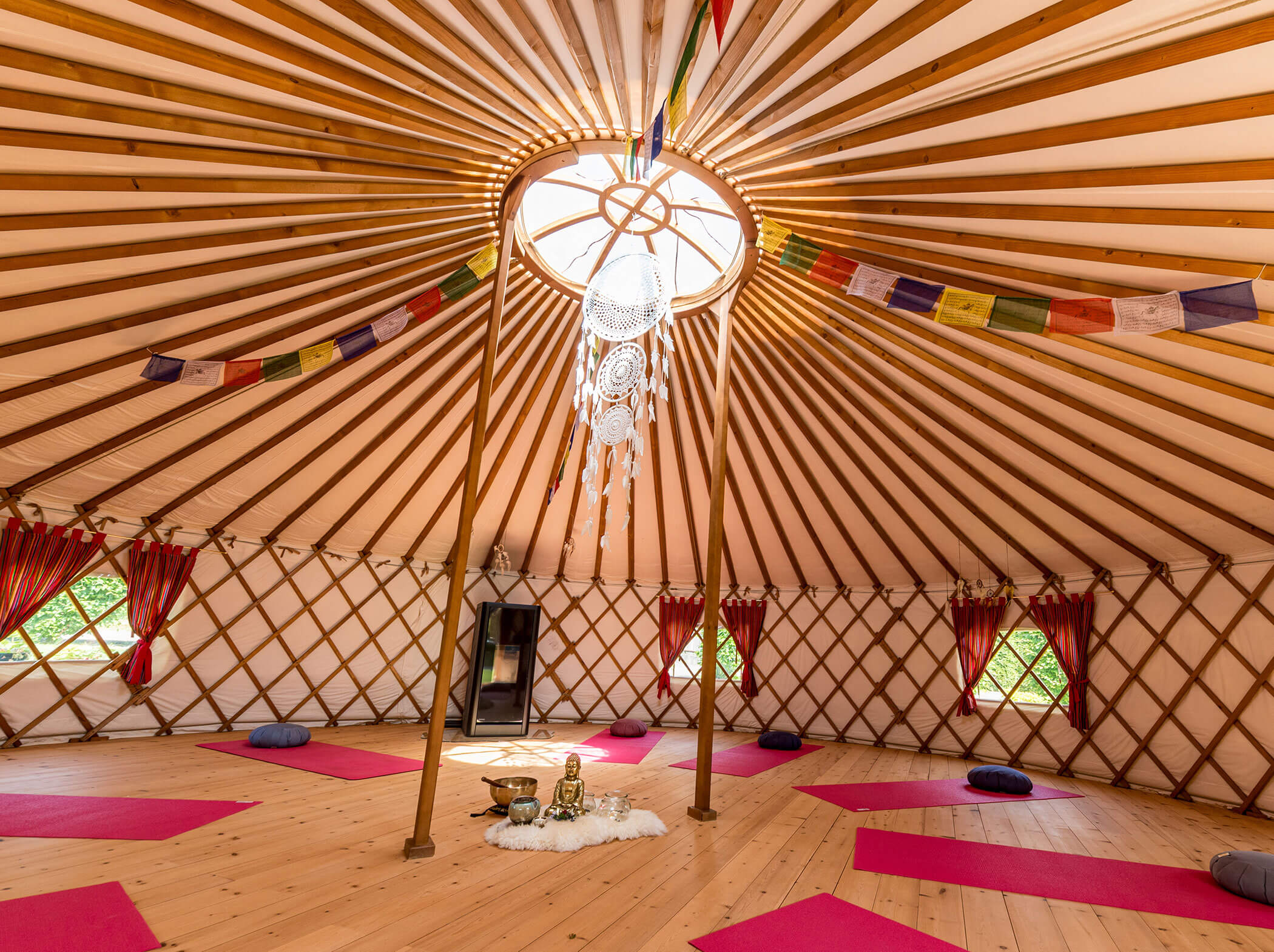 Das Innere einer geräumigen Jurte mit Yogamatten, Kissen, Gebetsfahnen und natürlichem Licht, das durch die zentrale Kuppel fällt. - Hotel Sun