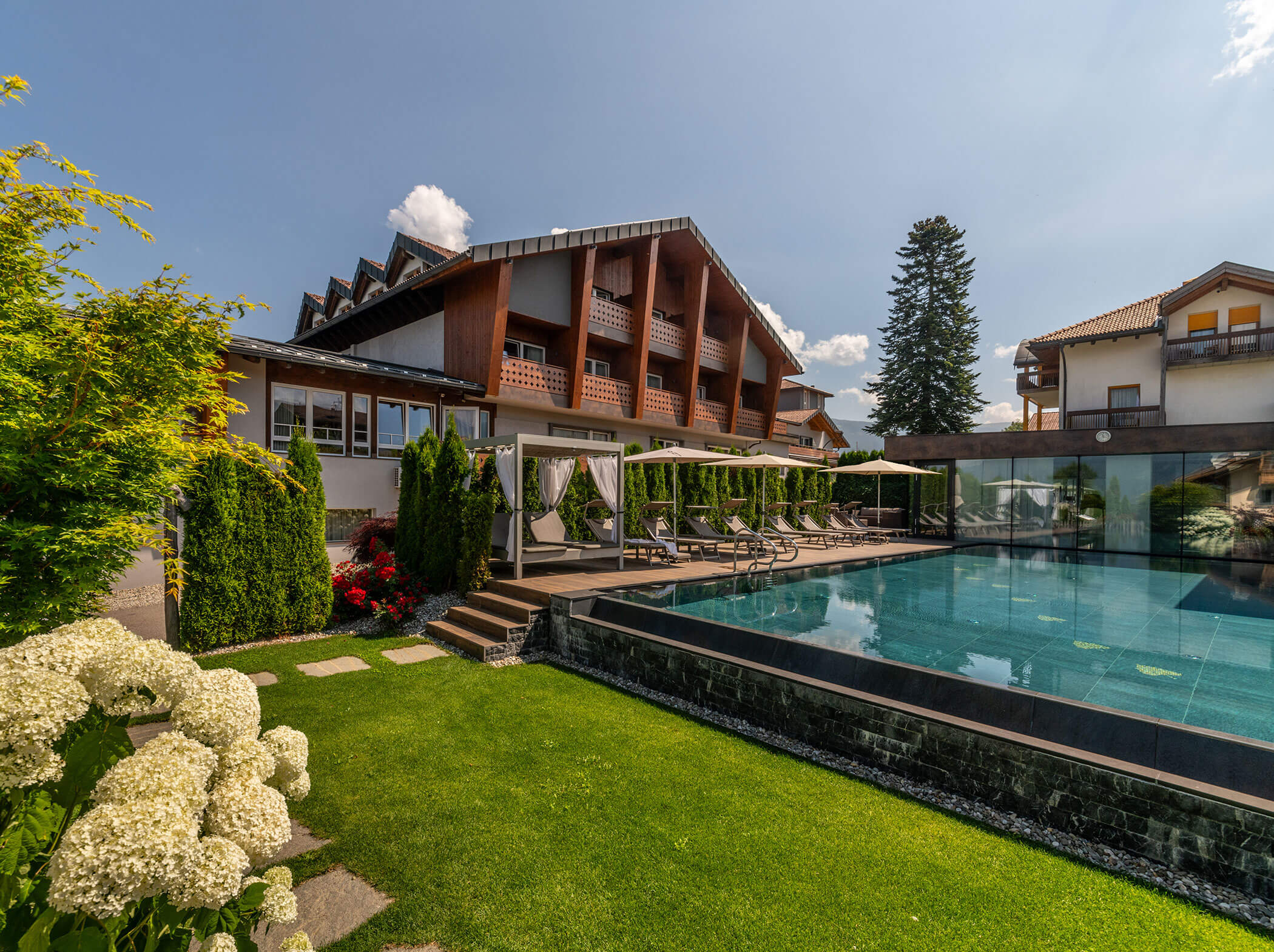 Modernes Hotel mit Balkonen und Pool, umgeben von Grün und Blumen an einem sonnigen Tag. - Hotel Sun