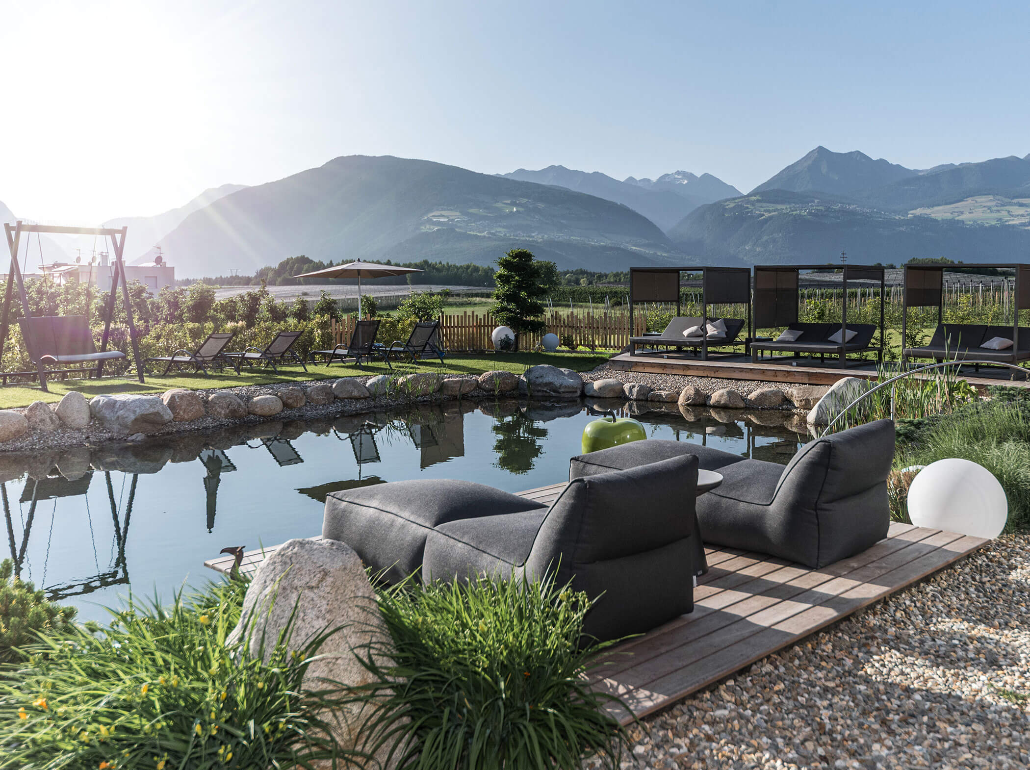 Moderne Loungesessel an einem natürlichen Teich mit Blick auf die Berge und die grüne Landschaft im Hintergrund. - Hotel Sun