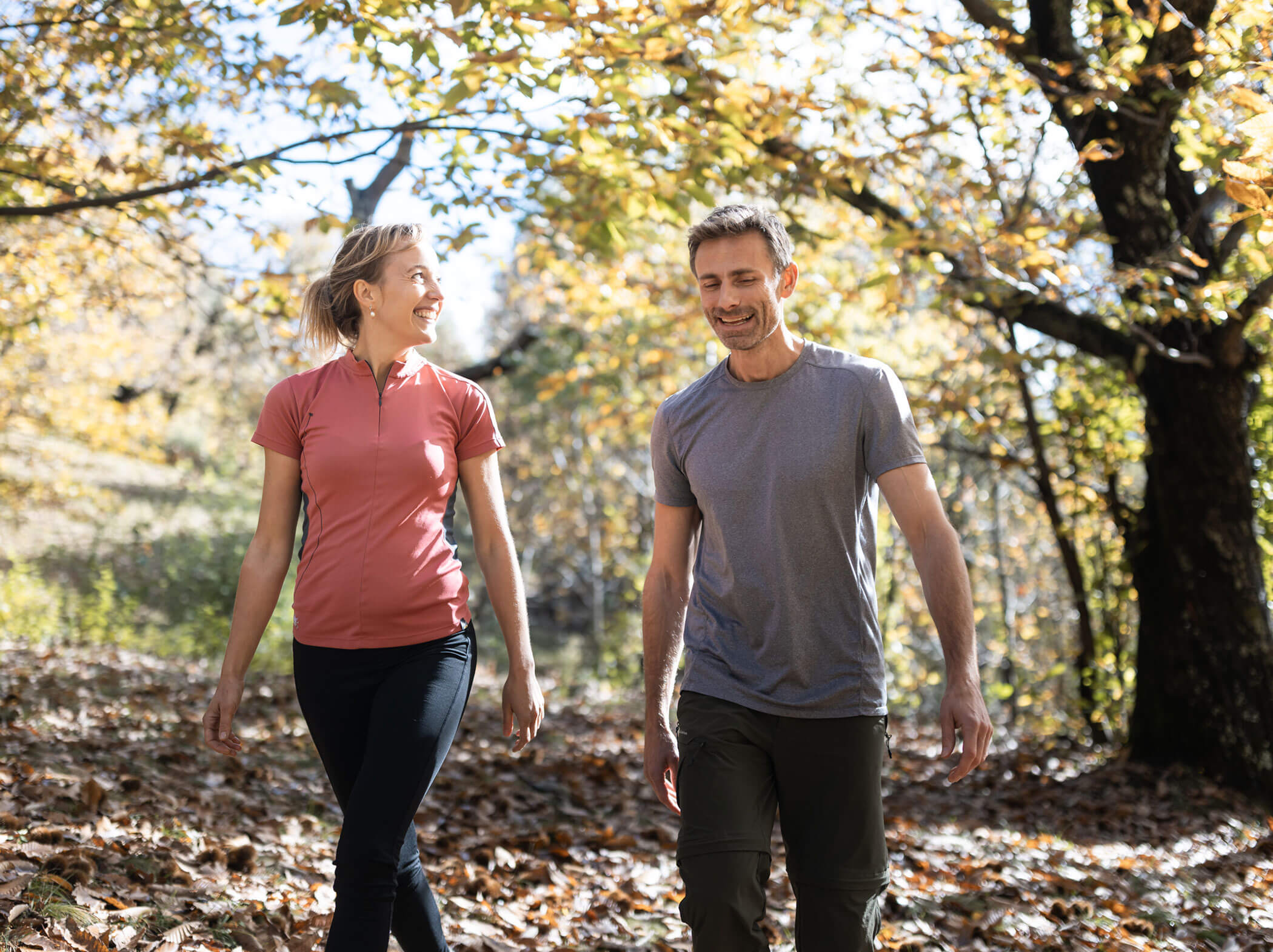 Zwei lächelnde Menschen, die zusammen auf einem grünen Weg in einem sonnenbeschienenen Wald im Herbst spazieren gehen. - Hotel Sun