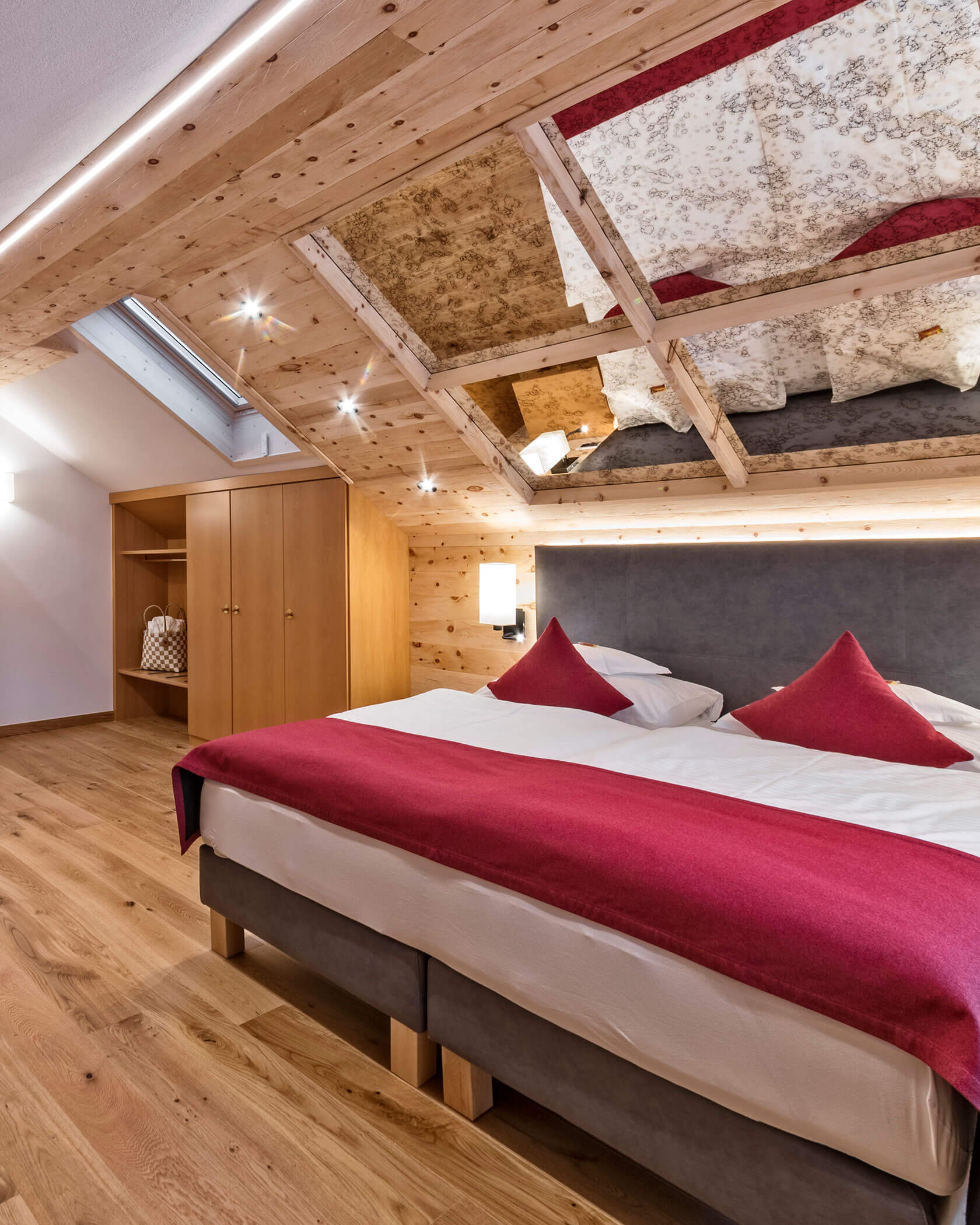 Gemütliches Schlafzimmer im Dachgeschoss mit Holzdekor, Doppelbett, roter Bettwäsche, offenem Kleiderschrank und einem Dachfenster. - Hotel Sun