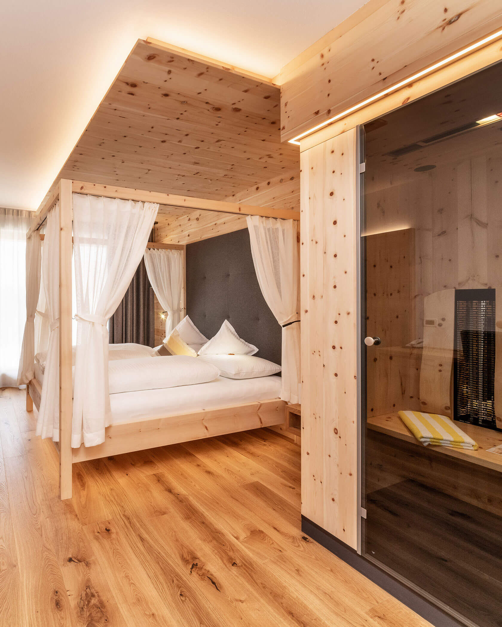 Ein gemütliches Holzschlafzimmer mit Himmelbett, weißen Vorhängen und einer verglasten Sauna auf einem Holzboden. - Hotel Sun
