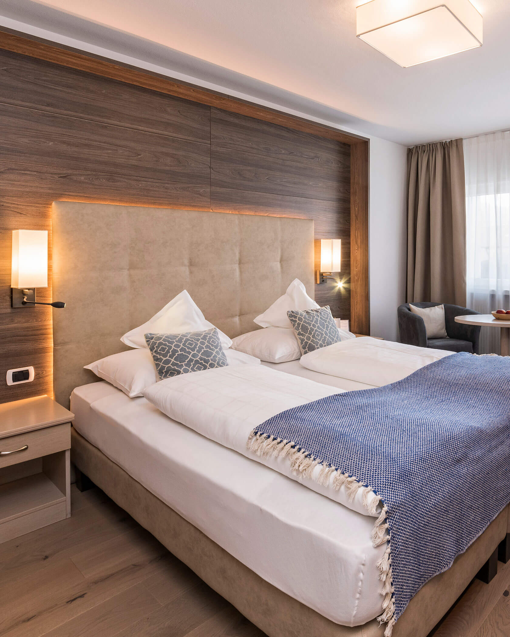 Ein modernes Hotelzimmer mit einem Doppelbett, einer blauen Decke, Nachttischen und warmer Beleuchtung. - Hotel Sun