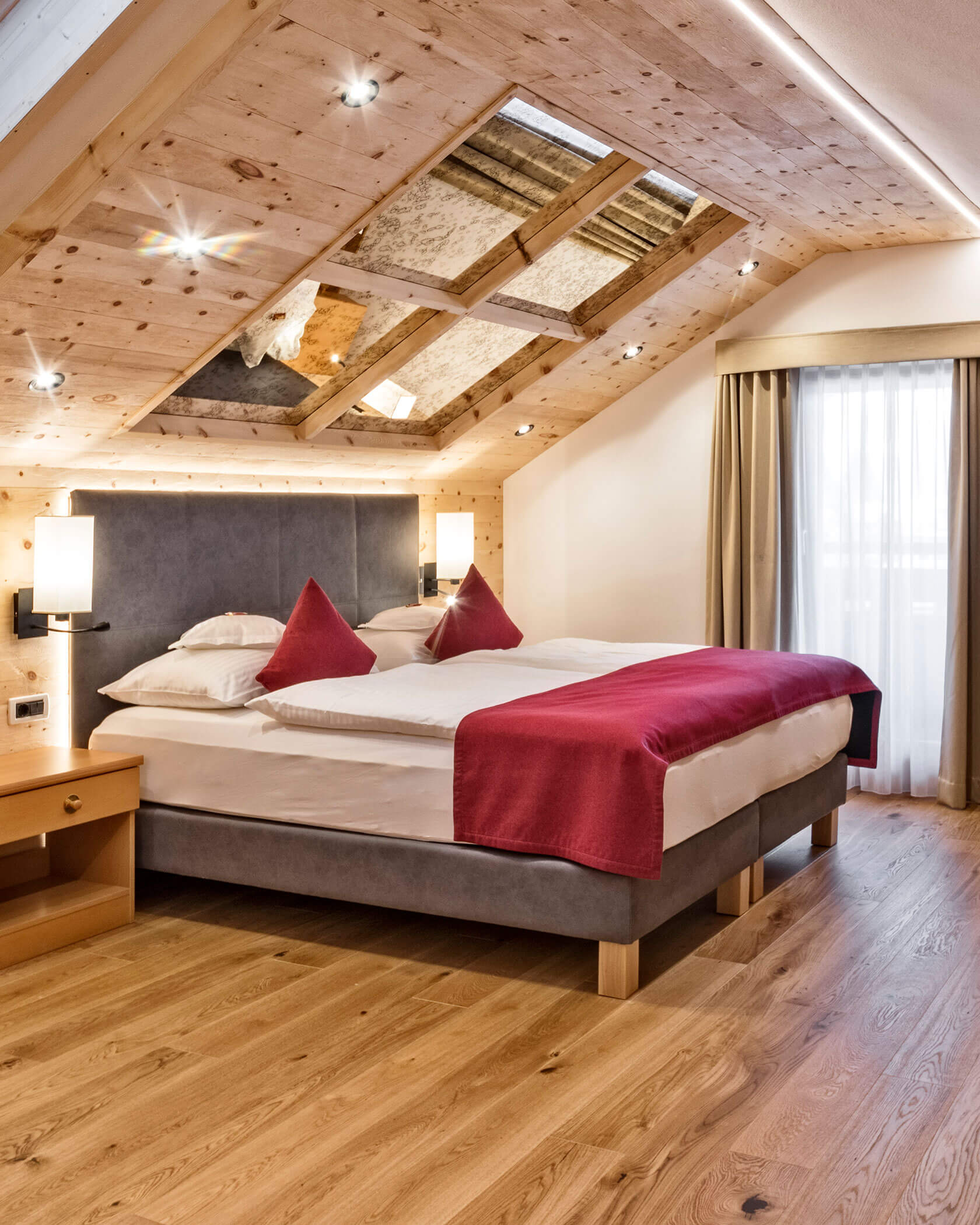 Gemütliches Schlafzimmer im Dachgeschoss mit einem Doppelbett, roten Akzenten, Holzböden und einem Oberlicht in der schrägen Decke. - Hotel Sun