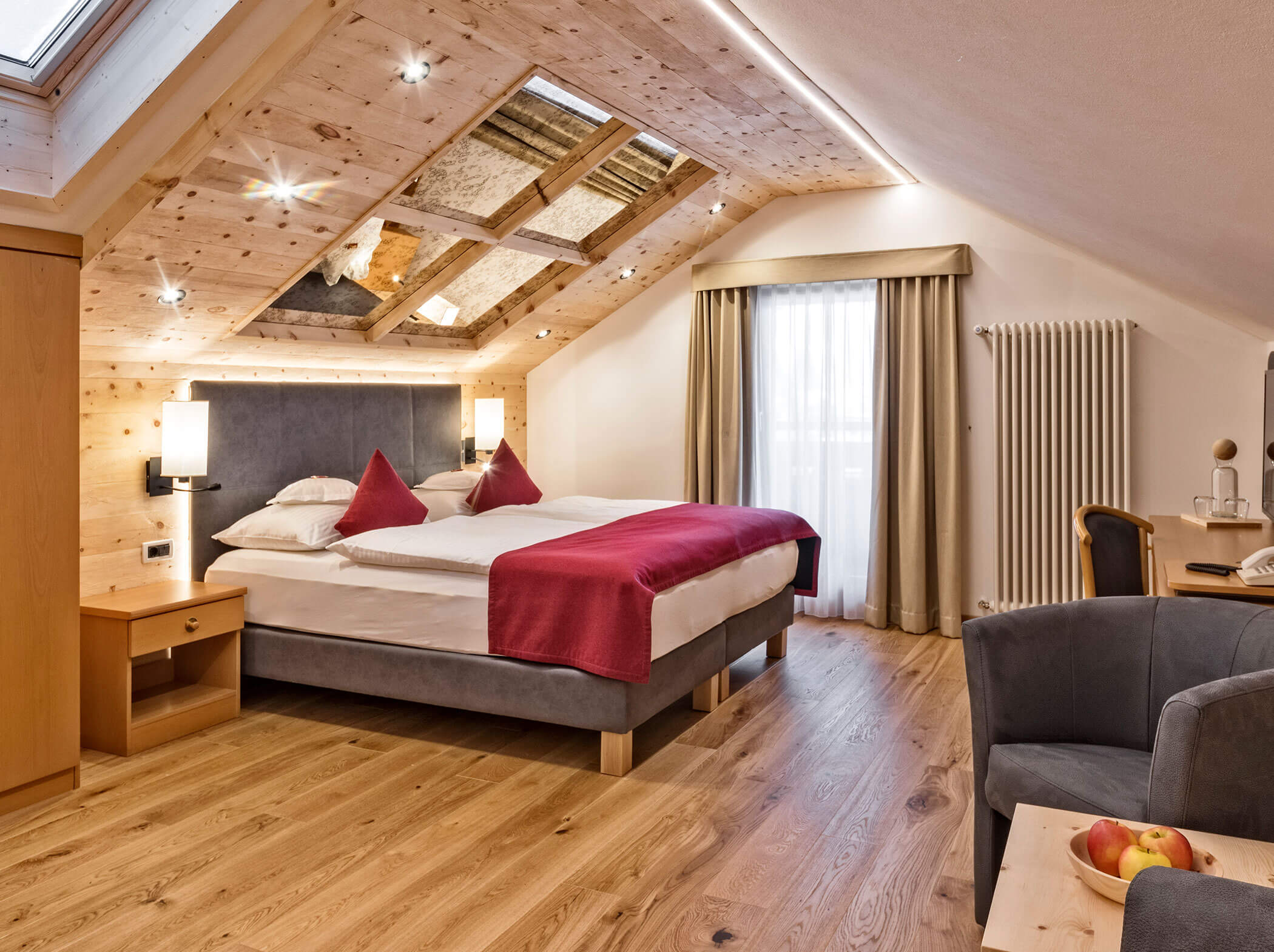 Gemütliches Hotelzimmer mit Doppelbett, roten Akzenten, Holzfußboden, schräger Decke und Oberlichtfenster. - Hotel Sun